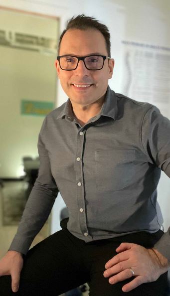 A man in glasses sitting on a stool in a chiropractic office.