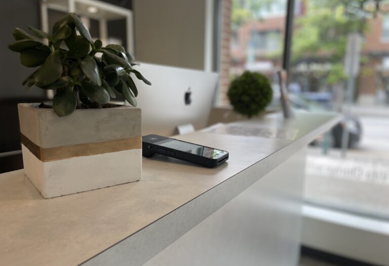 A smartphone and a potted plant sit on a white countertop in a modern office with a large window, ready for another productive day of billing tasks.