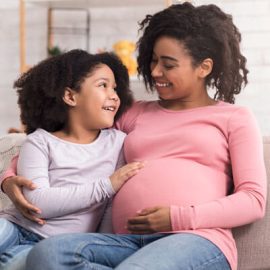 A pregnant woman and her daughter sitting on the couch.